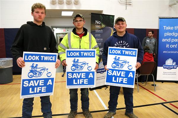 Three students hold "look twice save a life" signs. Three students hold "look twice save a life" signs.